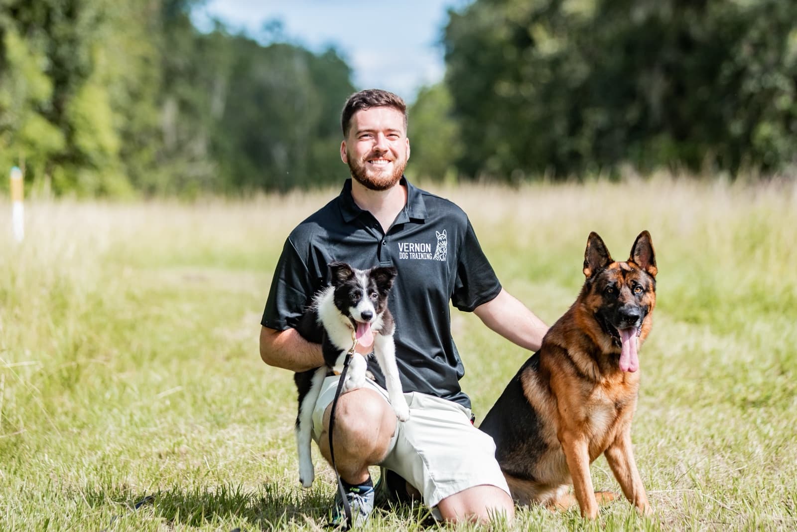 Trainer Ben Vernon kneeling in a field with a Border Collie and a German Shepherd
